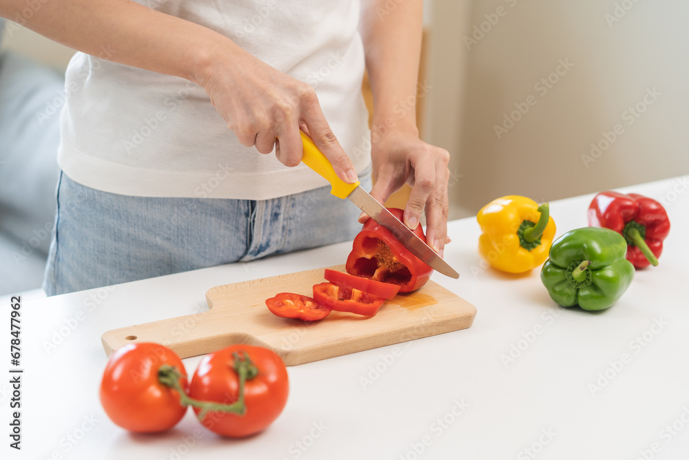Cooking healthy diet food with capsicum, hand of housewife asian young woman cutting red bell pepper cutting on wood board by knife in kitchen at home, fresh vegetable from nature organic for wellness Cooking healthy diet food with capsicum, hand of housewife asian young woman cutting red bell pepper cutting on wood board by knife in kitchen at home, fresh vegetable from nature organic for wellness