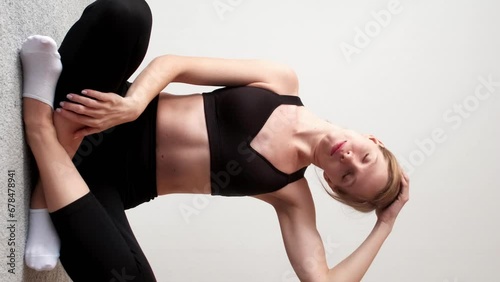 Vertical video. Home yoga. Morning sport. Flexibility training. Relaxed athletic woman stretching neck sitting cross-legged on light free space background.