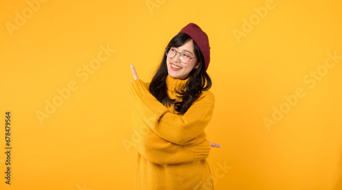 A cheerful woman in her 30s, wearing a red beret and eyeglasses, joyfully pointing her finger to free copy space against a bright yellow background. © Jirawatfoto