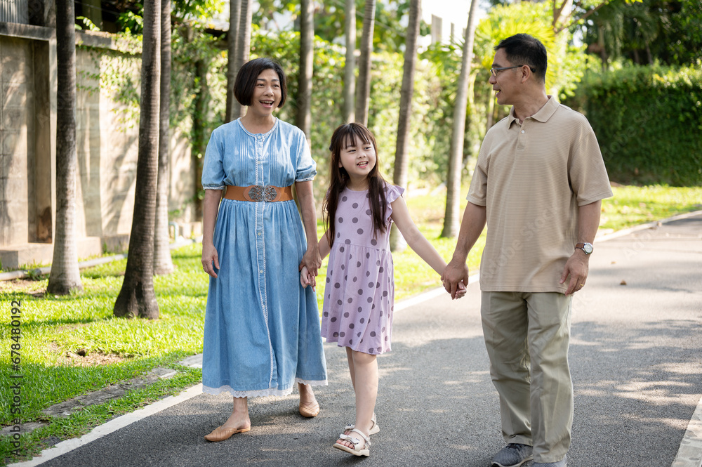 Caring Asian grandparents are holding their granddaughter's hands while strolling in a park together Caring Asian grandparents are holding their granddaughter's hands while strolling in a park together