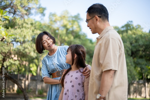 Kind Asian grandparents are having fun with their granddaughter, strolling around the park together. © bongkarn