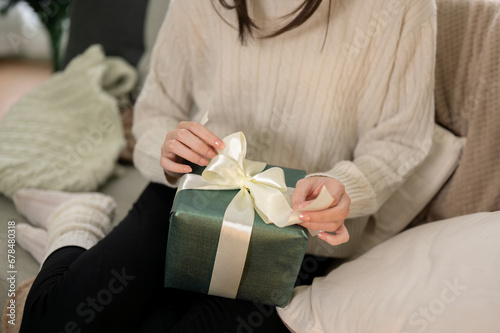 Close-up image of a woman is unwrapping a Christmas gift on a couch in her living room on Christmas