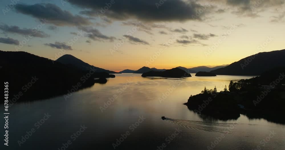 Aerial view of small boat traveling through golden sunlight and silhouetted peninsulas in Elaine bay in Pelorus Sound Te Hoiere of Marlborough Sounds, South Island of New Zealand Aotearoa Aerial view of small boat traveling through golden sunlight and silhouetted peninsulas in Elaine bay in Pelorus Sound Te Hoiere of Marlborough Sounds, South Island of New Zealand Aotearoa