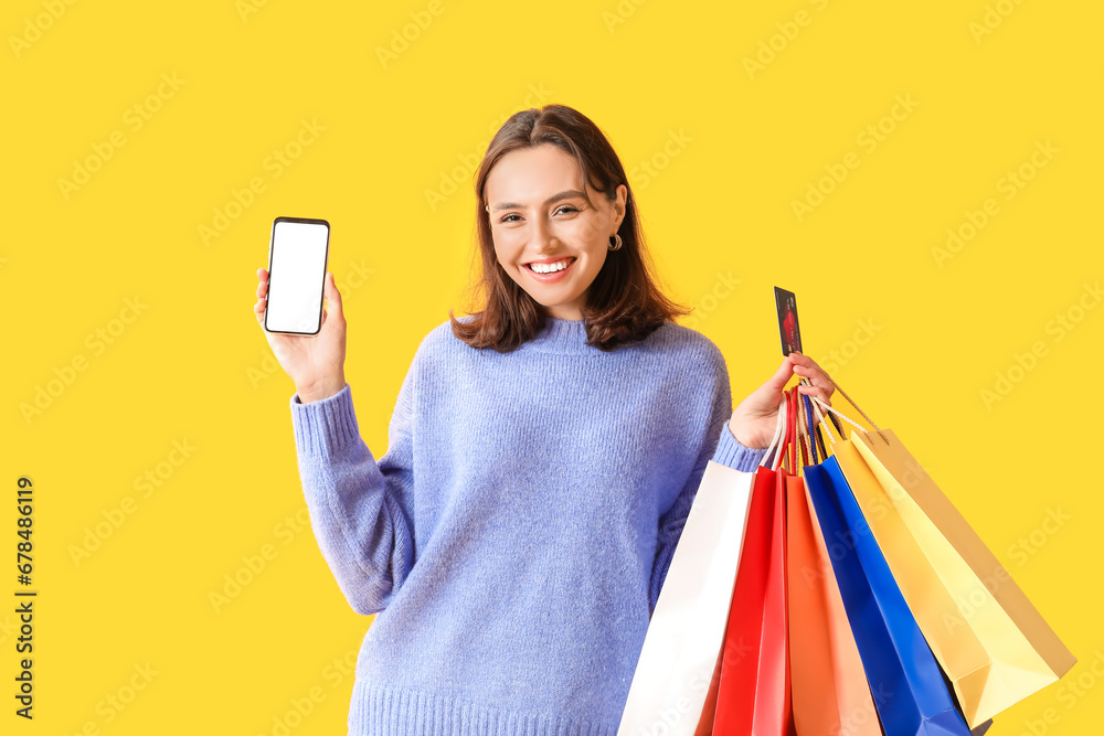 Young woman with credit card, mobile phone and shopping bags on yellow background - obrazy, fototapety, plakaty 