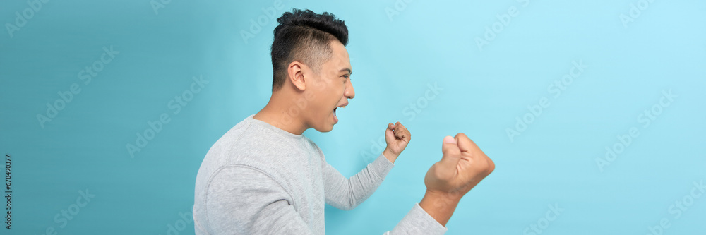 Young handsome man clenching fists like winner raised on blue banner Young handsome man clenching fists like winner raised on blue banner