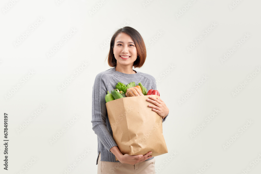 Smiling woman holding a shopping bag full of groceries posing on a studio white background. Smiling woman holding a shopping bag full of groceries posing on a studio white background.