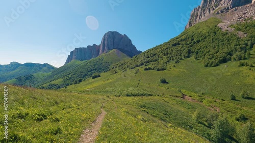 View of the mountains and the trail leading to the high cliffs. Hiking in summer. The mountains are covered with green grass. The sky above the steep cliffs is blue photo