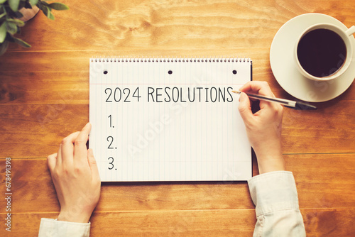 2024 Resolutions with a person holding a pen on a wooden desk