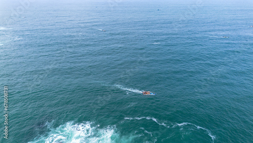 Drone view of Menganti Beach with white sand, calm waves, cliffs and green trees and the activities of traditional fishermen and traditional fishing boats