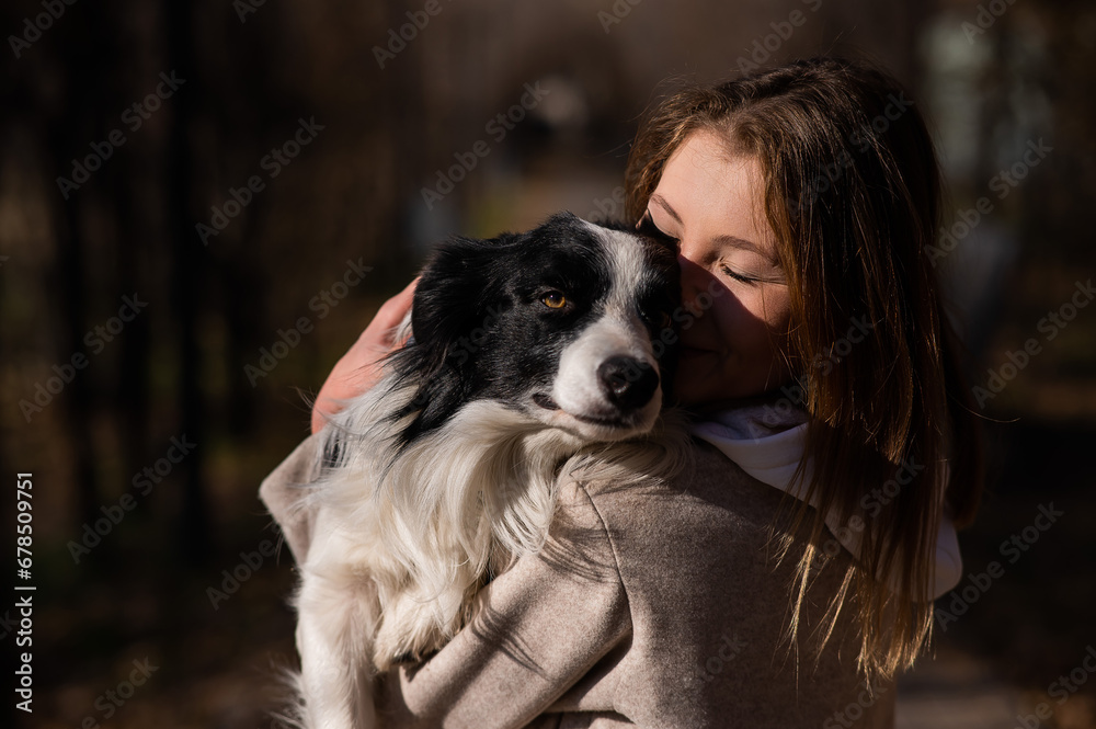 Caucasian woman holding a border collie in her arms while walking in the autumn park. Portrait of a girl with a dog. Caucasian woman holding a border collie in her arms while walking in the autumn park. Portrait of a girl with a dog.