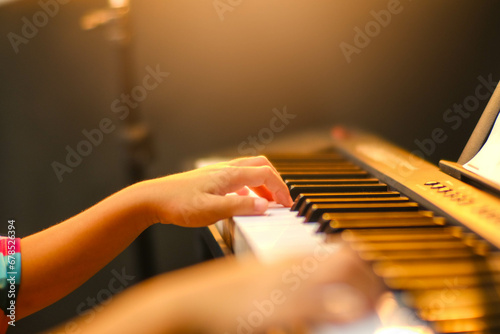 Close-up of a little student's hand playing the piano. Happy young Asian girl learning and practicing the piano. Selective focus.