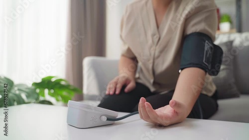 The woman is measuring her blood pressure by herself using a portable blood pressure monitor sitting on the sofa in the living room at home. Healthcare and medical concept. photo