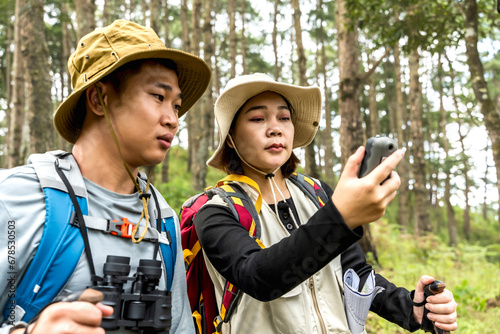 Young adventourous Asian couples hiking in the woods, woman hiker looking at GPS tools in forest