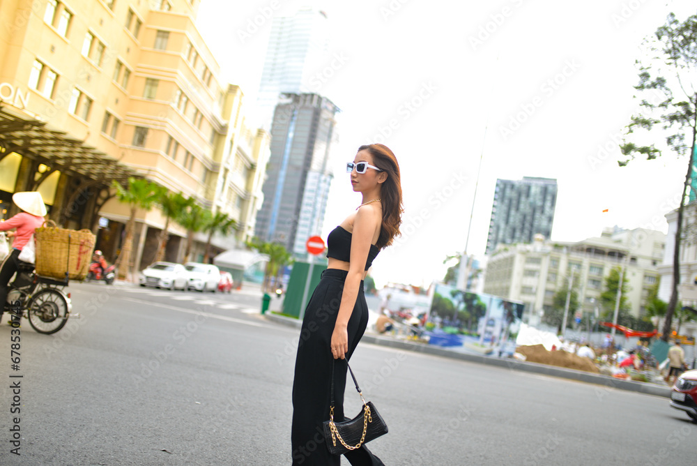 Fototapeta premium Young woman wearing sunglasses in city, colorful buildings and feel the warm. Exploring this bustling metropolis is a true adventure