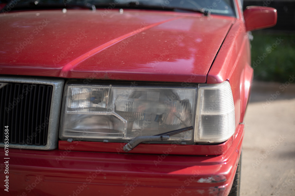 In front of car. Red car in parking lot. Front wiper on headlight.