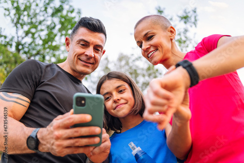 sporty family using a mobile phone and smart watch to plan their sports training in the countryside, concept of sport with kids in nature and active lifestyle