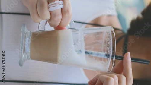 vertical shot. close-up of a glass of latte. The girl holds a glass of latte and drinks it through a straw. photo