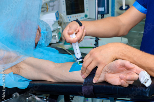 An anesthesiologist injects intravenous anesthesia with a large syringe into the patient's arm on the operating table. Surgery with general anesthesia. photo