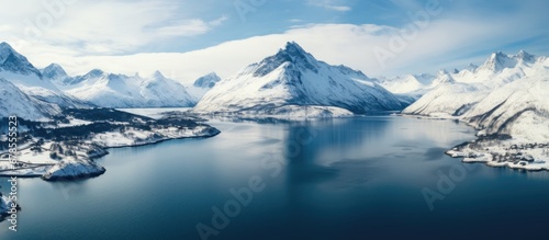 A wide lake nestled amidst snow capped mountains seen from above © Vusal