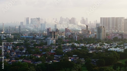Mumbai suburban cityscape with buildings, factories with smoke chimneys, slums and metro rail passing. Indian city with factories close to residential buildings polluting the air.