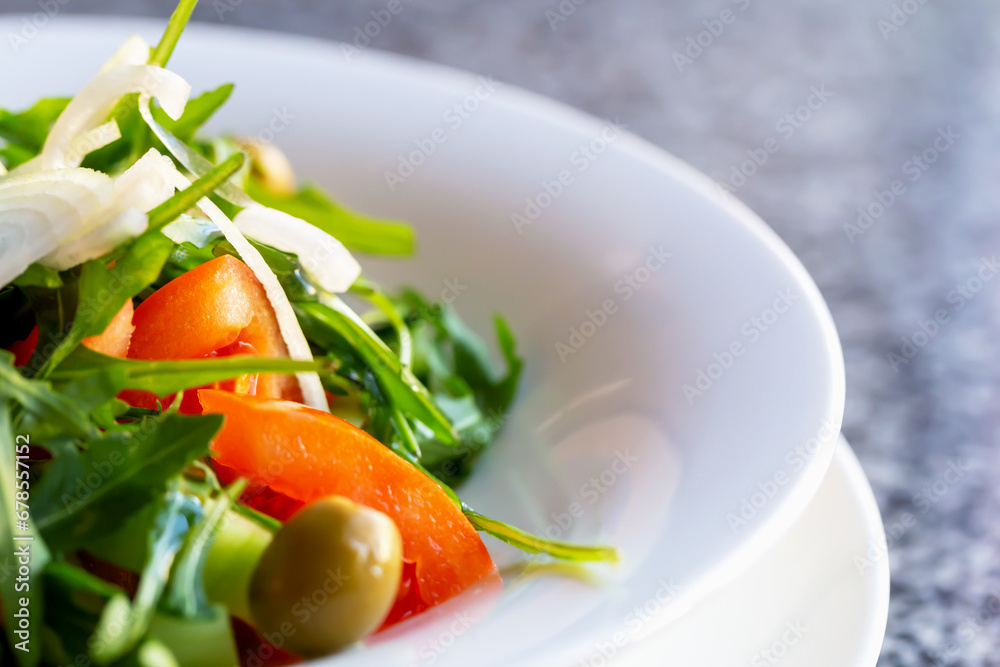 Fresh delicious healthy salad with arugula, tomato and onion, cucumber and olive in plate on the table close-up. Proper nutrition. Diet and health. Selective focus, defocus Fresh delicious healthy salad with arugula, tomato and onion, cucumber and olive in plate on the table close-up. Proper nutrition. Diet and health. Selective focus, defocus