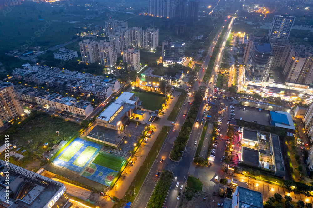 Fototapeta premium aerial drone shot showing brightly lit street with multi story sky scrapers offices, homes, shopping malls, sports arenas and more in metropolitan city like gurgaon, delhi, mumbai, bangalore