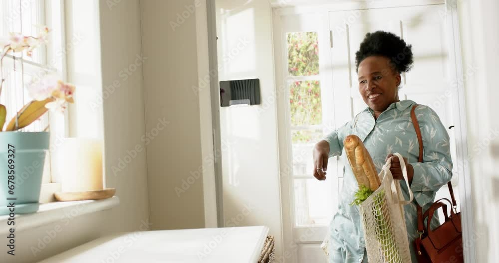 Happy african american senior woman entering house with shopping in sunny room, slow motion