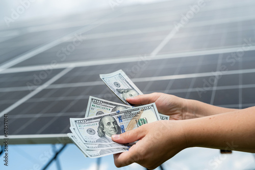 young hands holding a large amount of dollars against solar panel