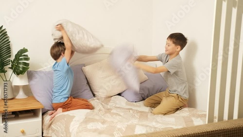 Two boys are fighting with pillows at home on the bed.