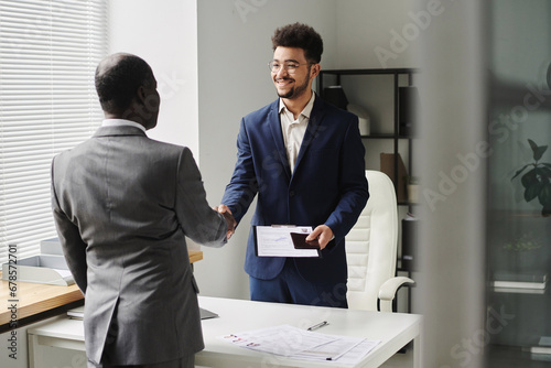 Specialist of visa center congratulating man of getting visa, they standing and shaking hands photo