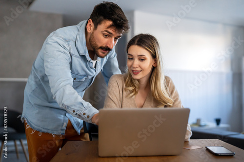 Portrait of a smiling couple looking at laptop together at cozy home office.