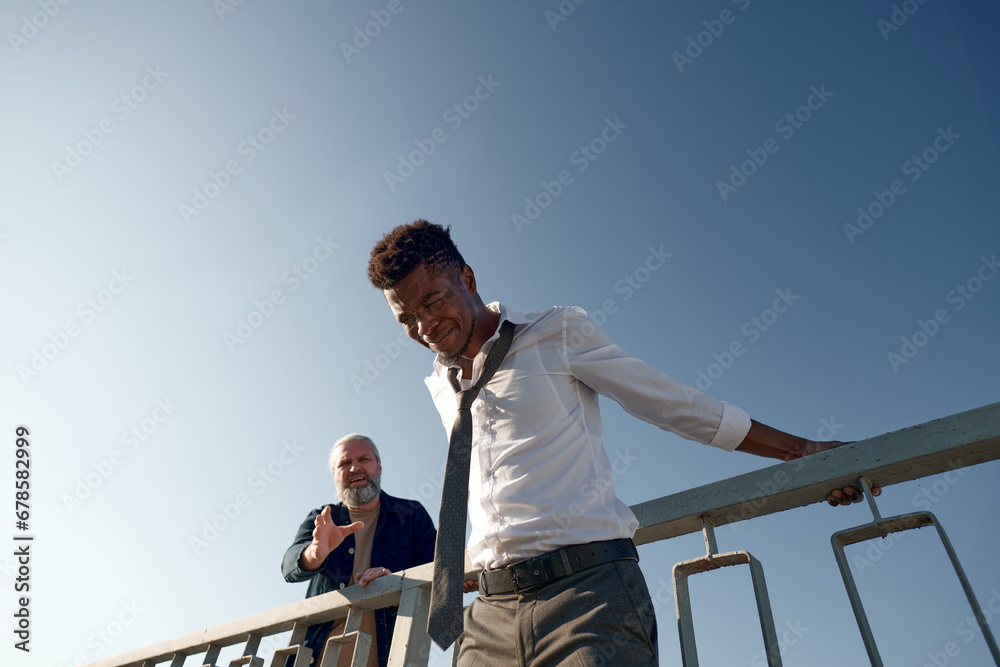 African American young man in depression getting ready for jump fro the bridge while other man trying to stop him in background