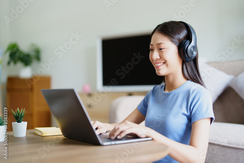 woman wearing headphones on comfortable couch listening to using computer laptop and music. © Jirapong