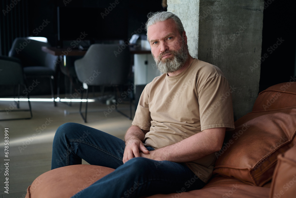 Portrait of bearded mature man looking at camera while sitting on sofa in the living room Portrait of bearded mature man looking at camera while sitting on sofa in the living room