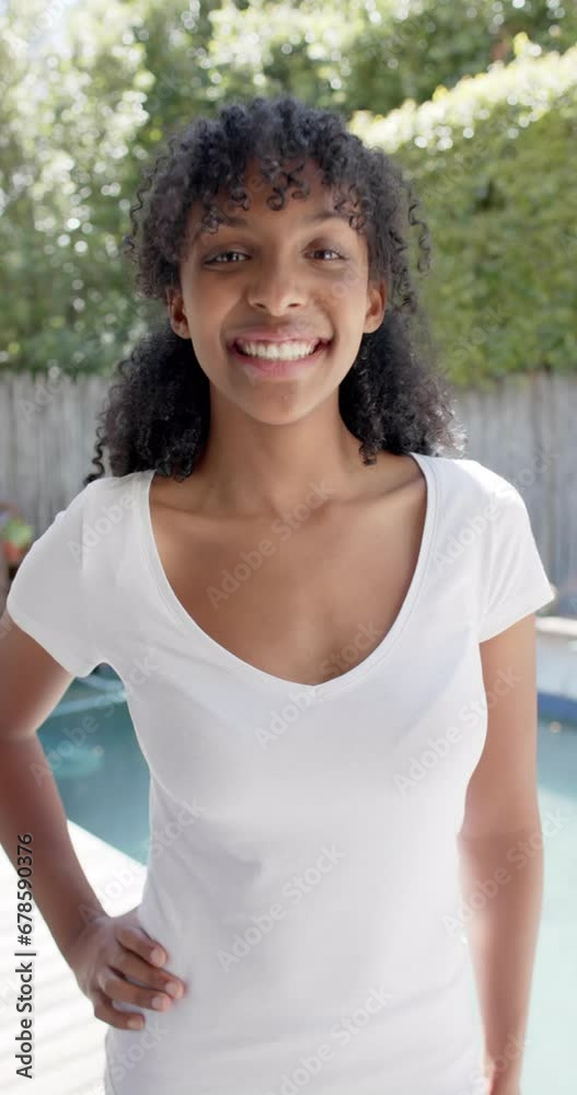 Vertical video of happy biracial woman in white t shirt, smiling in sunny garden, slow motion Vertical video of happy biracial woman in white t shirt, smiling in sunny garden, slow motion
