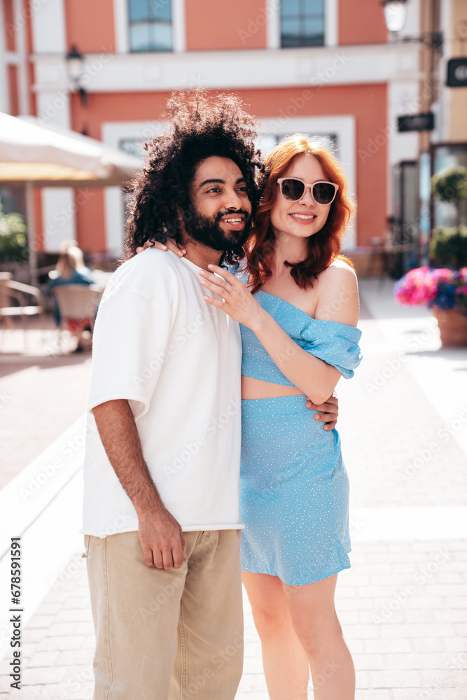 Smiling beautiful redhead  woman and her handsome boyfriend. Model in casual summer clothes. Happy cheerful family. Female having fun. Couple posing in the street at sunny day. In sunglasses