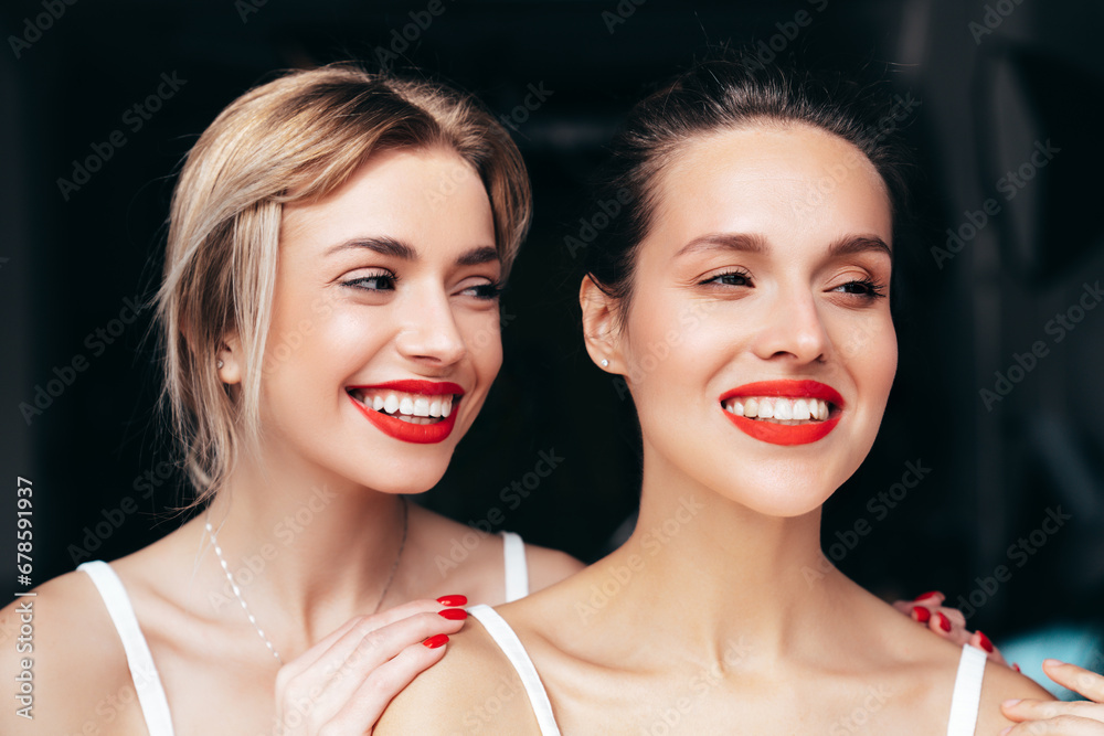 Closeup portrait of two young beautiful smiling brunette female with glamour evening makeup. Sexy women with healthy glowing face skin. Hot models with red lips posing over dark background Closeup portrait of two young beautiful smiling brunette female with glamour evening makeup. Sexy women with healthy glowing face skin. Hot models with red lips posing over dark background