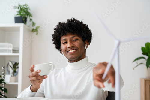 Smiling businessman holding tea cup and touching wind turbine model photo
