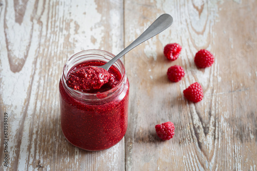 Jar of raspberry jam on wooden surface photo