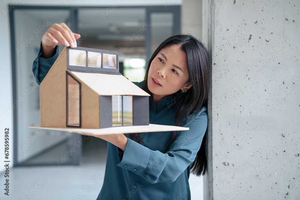 Businesswoman examining model house in office corridor Businesswoman examining model house in office corridor