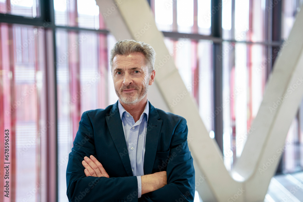 Smiling businessman standing with arms crossed in front of window Smiling businessman standing with arms crossed in front of window