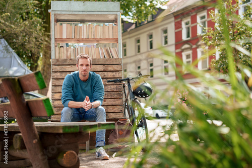 Man sitting on bench near cabinet of books near plants photo