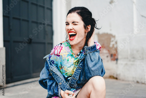 Young woman wearing denim jacket and laughing near wall photo