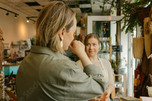 Woman choosing perfume by smelling on hand by owner in store photo