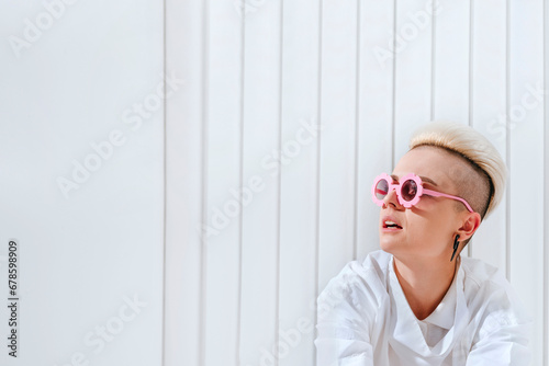 Thoughtful woman wearing funky glasses in front of white wall photo
