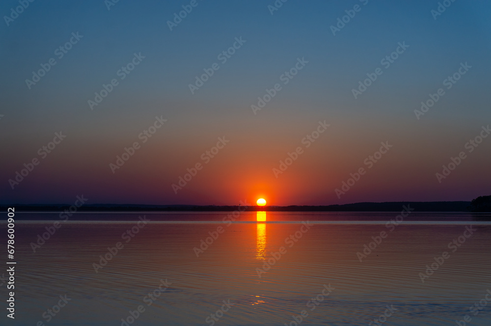 sunset over the sea or lake. Bright orange sun with a ray on the water.
