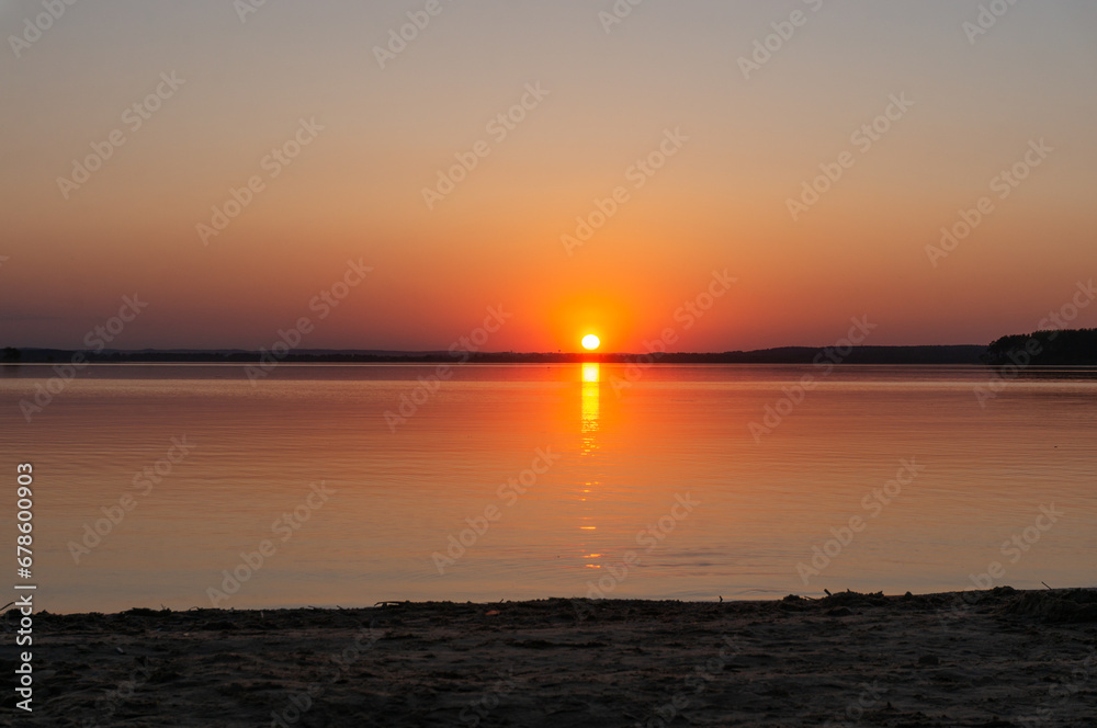 sunset over the sea or lake. Bright orange sun with a ray on the water..