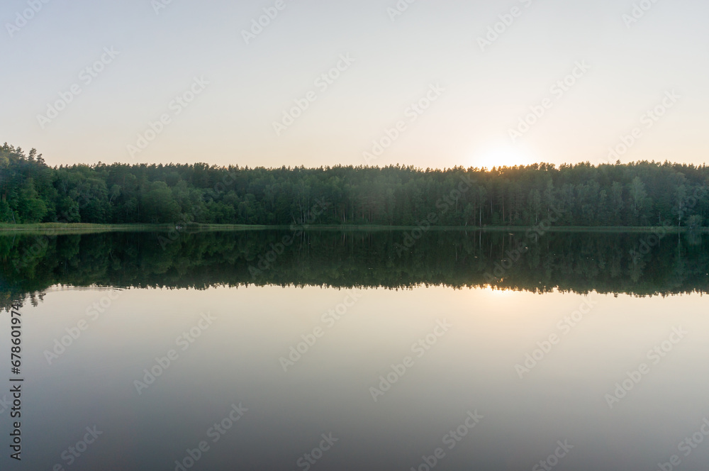 Lake surrounded by trees that reflect in the water. Fog on the surface of the forest