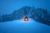 Isolated wooden cottage amid snow-laden conifers on a mountain clearing hidden within the forest in the winter. Christmas holiday and winter vacations concept