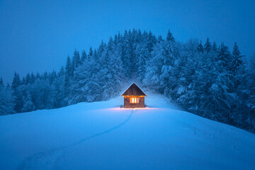 Isolated wooden cottage amid snow-laden conifers on a mountain clearing hidden within the forest in the winter. Christmas holiday and winter vacations concept